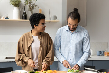 Happy sincere affectionate young married African American family couple enjoying preparing healthy weekend meal together in modern kitchen, chopping organic vegetables for salad, culinary hobby.