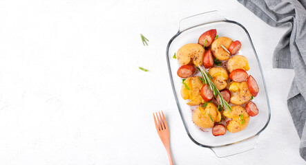 Smashed potato with sausage and herbs roasted in the glass dish on the white table. Hot meal. Copy space