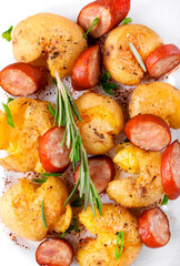 Smashed potato with sausage and herbs roasted in the glass dish. Hot meal. Top view