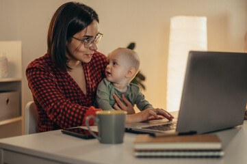 Beautiful business mom using a laptop and spending time with her baby boy at home