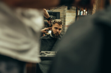 Fototapeta na wymiar Young bearded man getting haircut by hairdresser