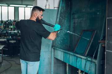 Male worker cleaning screen frame with water in a printing workshop