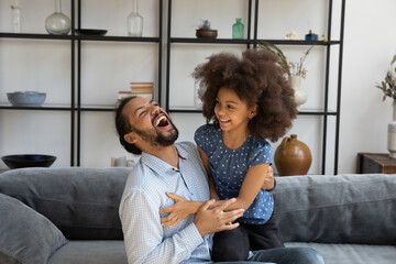 Joyful laughing young African American father tickling emotional happy adorable small child...