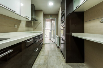 Kitchen with smooth stone countertop with ceramic hob with extractor hood and appliances, dark cabinets and cream stoneware