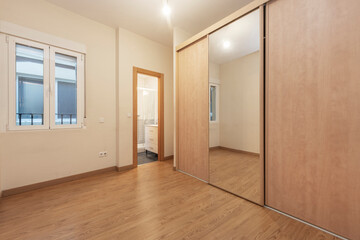 Empty furniture room with built-in wardrobe with large mirror door and separate toilet and view of hallway