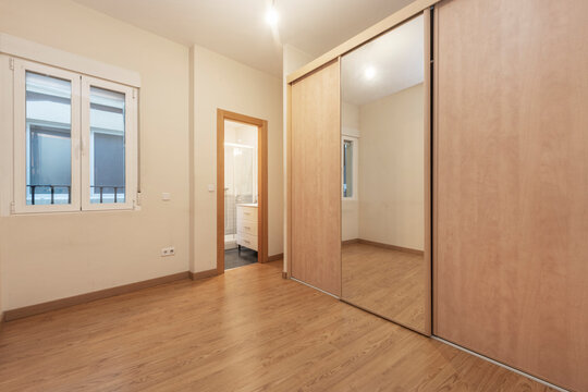 Empty furniture room with built-in wardrobe with large mirror door and separate toilet and view of hallway