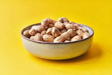  Bowl of peanuts with shell on a yellow background