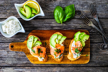 Tasty sandwiches - toasted bread with cream cheese, smoked salmon, avocado and parsley on wooden...