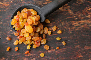 sweet, yellow raisins in a black spoon on a wooden plate.