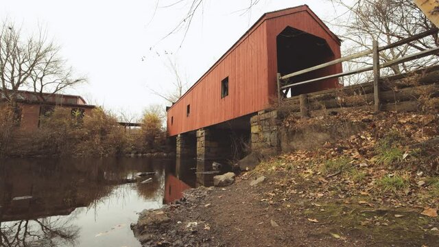 Covered bridge at Eli Whitney Museum & Workshop  Hamden Connecticut over the mill river on a cloudy day. A lattice truss bridge designed by Ithiel Town with a gentle flow of water under it.