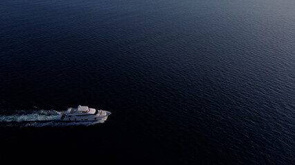 White luxury yacht sails on the ocean. Shooting from a drone as a small light sea vessel, leaving a trail of foam and waves along the sea dark water surface