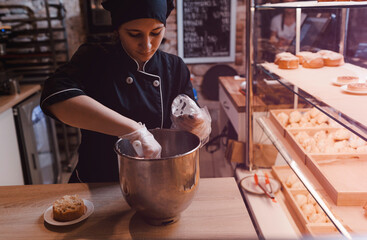 a cook girl in a black suit puts cream in a pastry bag. The pastry chef puts cream in a cooking bag from a mixer.