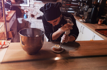 a pastry chef girl decorates a shortbread cake with a pastry bag with protein cream, squeezes out the cream. Close-up