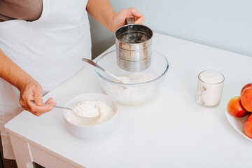 Senior woman cook preparing pie dough at home kitchen. Close-up of female hands pouring flour into bowl