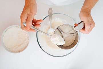 Top view of woman cook preparing dough for baking at home kitchen. Close-up of female hands pouring flour into bowl. Selective focus on spoon with flour. Home cooking hobby
