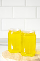 Two jars of clarified ghee butter on kitchen tile background, wooden plank.