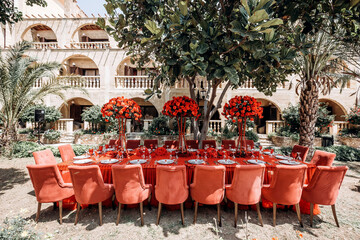 red table wedding arrangement of roses, carnations on the background of a table with a red tablecloth, red chairs and a tree in summer