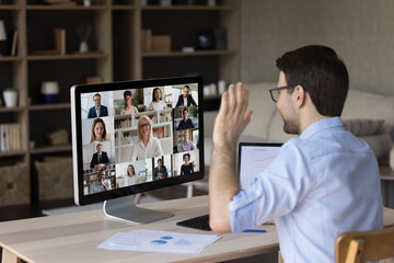 Obraz na płótnie Canvas Millennial office employee meeting, talking to business team on video call, negotiating with office coworkers on online virtual conference chat, waving hand hello at monitor, discussing project