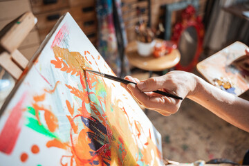 Female artist holding brush and drawing with paints on the canvas at her flat
