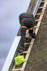 A man works on the roof repair, installs sheet metal on top of the gable wall