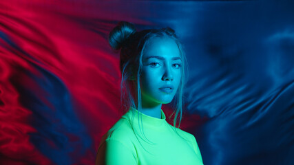Pretty face of stylish young teen girl in changing colorful neon light on waving backdrop