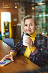 Beautiful middle-aged caucasian woman chatting on social media during a coffee break at a coffee shop.