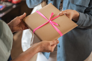 Young girl standing in front her mature tutor and giving present with pink ribbon to her