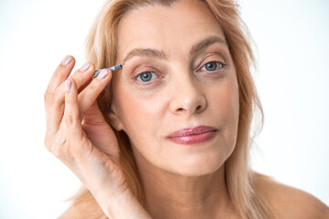 Obraz premium Mature woman with nude makeup plucking eyebrows