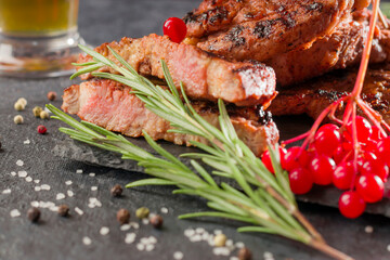 Close-up juicy meat, grilled, barbecue. Hot steak with rosemary, salt, pepper, red berries on a stone board.