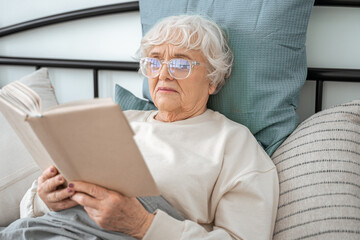 Fototapeta na wymiar Senior woman holding book, while reading her favorite novel at home