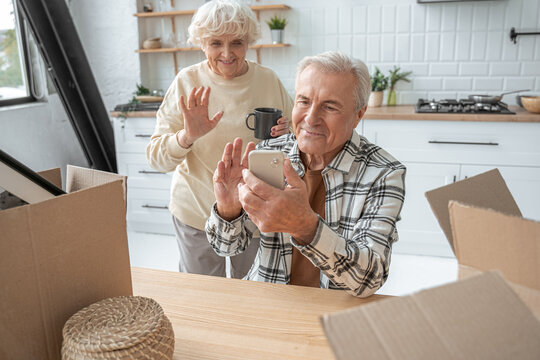 Retirement man holding smartphone and waving while chatting with somebody