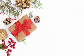 New Year concept. Gift box with red ribbon, pine branches, cones and Christmas ornaments on white. Space for text. Christmas background.
