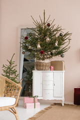 Decorated Christmas tree to the basket stands on a white classic chest of drawers in the living room
