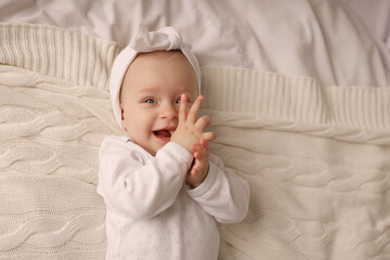 a 6-month-old baby lies in a crib in the nursery with white clothes on her back and laughs, looks...