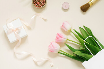 Flat lay composition with cosmetic products for makeup and pink tulips on a beige background
