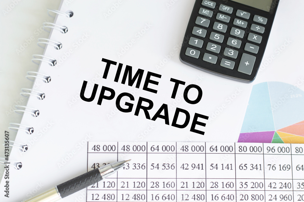 Poster text time to upgrade on a notepad on the office desk next to a calculator, charts and reports. busin