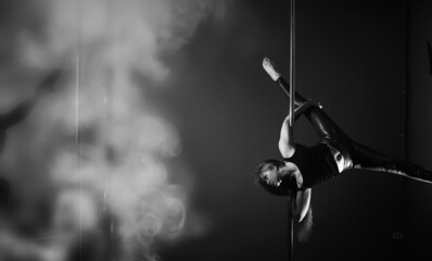 The dancer on the pylon in the studio. Girl doing exercises on a sports equipment.