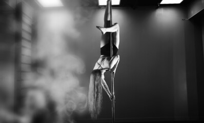 The dancer on the pylon in the studio. Girl doing exercises on a sports equipment.