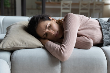 Close up unhappy depressed millennial woman lying on couch at home alone, thinking about personal problems, frustrated upset young female lost in thoughts, break up with boyfriend or divorce