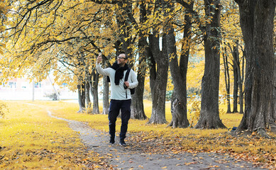 A young man in glasses walks in the park with an umbrella during the rain.