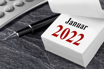 Finanzen und Kalender Januar 2022 mit Rechner und Kugelschreiber am Arbeitsplatz
