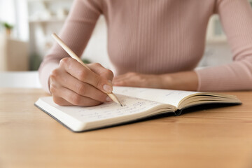 Close up cropped of woman taking notes in notebook, holding pencil, businesswoman entrepreneur planning workday in organizer, meetings, managing time, student preparing to exam, handwriting