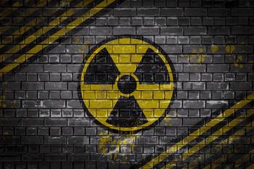 A shabby radiation sign depicted on a dark brick wall warning of radiation hazards