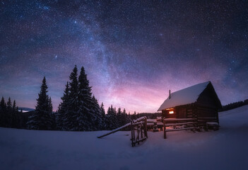 Paysage d& 39 hiver fantastique avec maison en bois dans les montagnes enneigées. Ciel étoilé avec voie lactée et hutte couverte de neige. Concept de vacances de Noël et de vacances d& 39 hiver