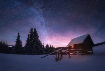 Foto op Plexiglas Fantastisch winterlandschap met houten huis in besneeuwde bergen. Sterrenhemel met Melkweg en besneeuwde hut. Kerstvakantie en wintervakanties concept © Ivan Kmit