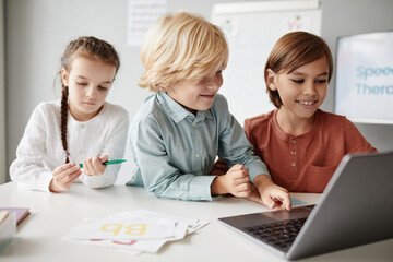 Group of children sitting at the table and typing on laptop during a lesson, they studying online