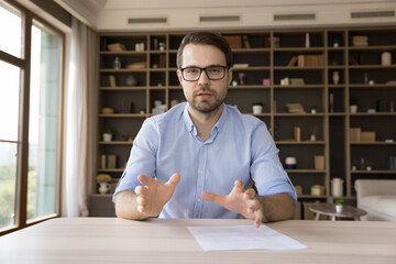 Serious confident millennial business professional in glasses looking at camera, holding online...