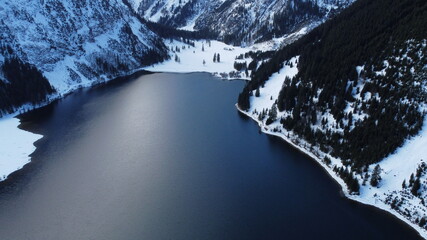 lago rodeado de montañas y bosque cubierto de nieve.