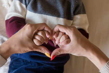 Heart shape created from young woman fingers. Infant hands on mother arms. Lovely emotional, sentimental moment. Closeup. Point of view shot.