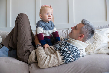 A happy father is having a good time with a charming son close-up, the family is having fun at home, a smiling dad hugs a little boy, plays a game, enjoys the weekend, having fun together